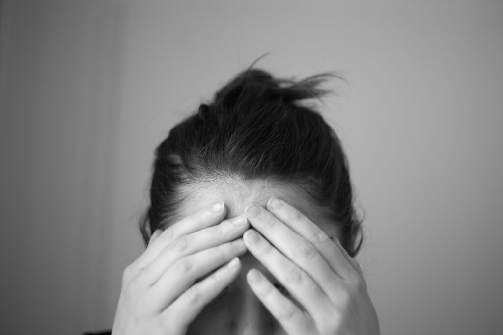 A black and white photo of a woman holding her head and covering her eyes as if experiencing a headache, taken by Jose Navarro