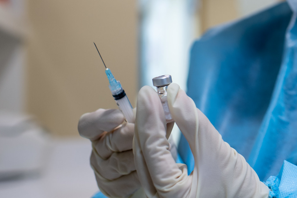 Gloved hands holding a vaccine vial and a needle and syringe