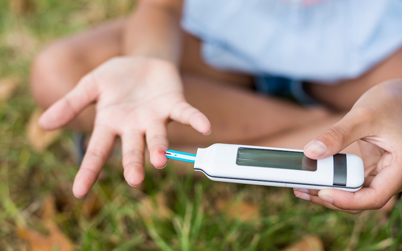 A child taking their blood sugar in a grass field