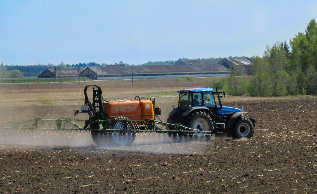 a tractor pulling an active pesticide tank and sprayer in a farm field, with mountains in the background