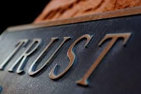 Close-up image of the word 'Trust' engraved on a dark metallic surface